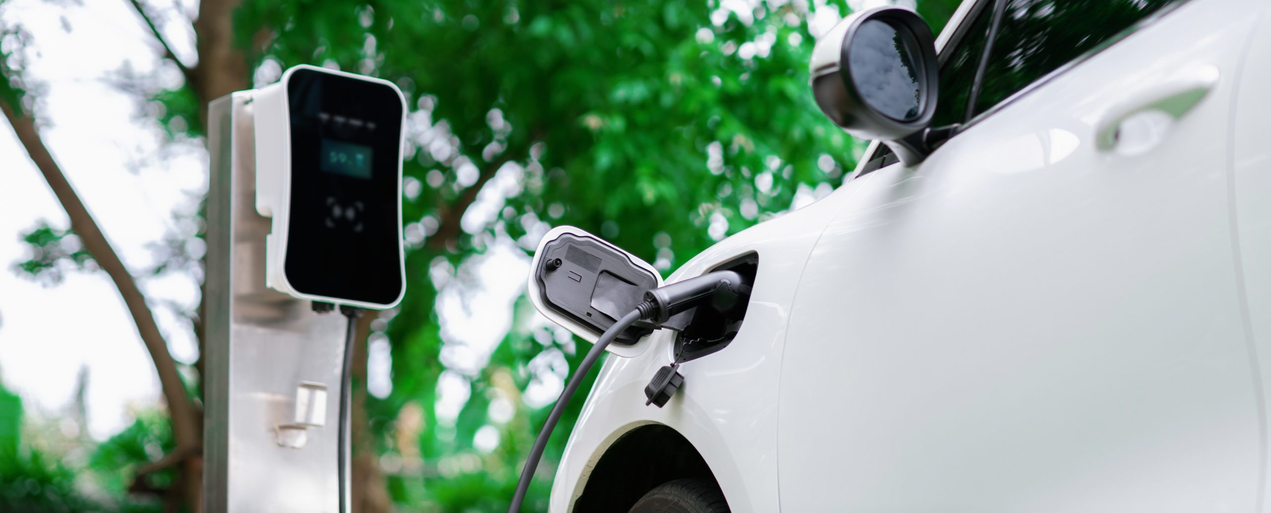 Focus closeup electric vehicle plugged in with EV charger device from blurred background of public charging station powered by renewable clean energy for progressive eco-friendly car concept.